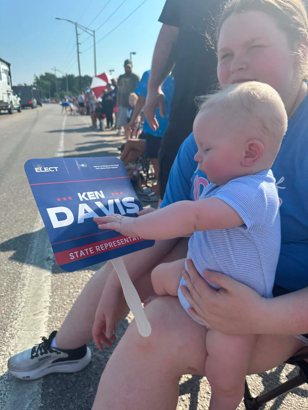 A young supporter holding a Ken Davis campaign hand fan along the parade route